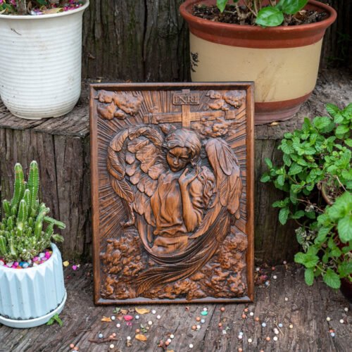 Female Angel wood relief displayed outdoors with plants, showing handcrafted wooden angel artwork