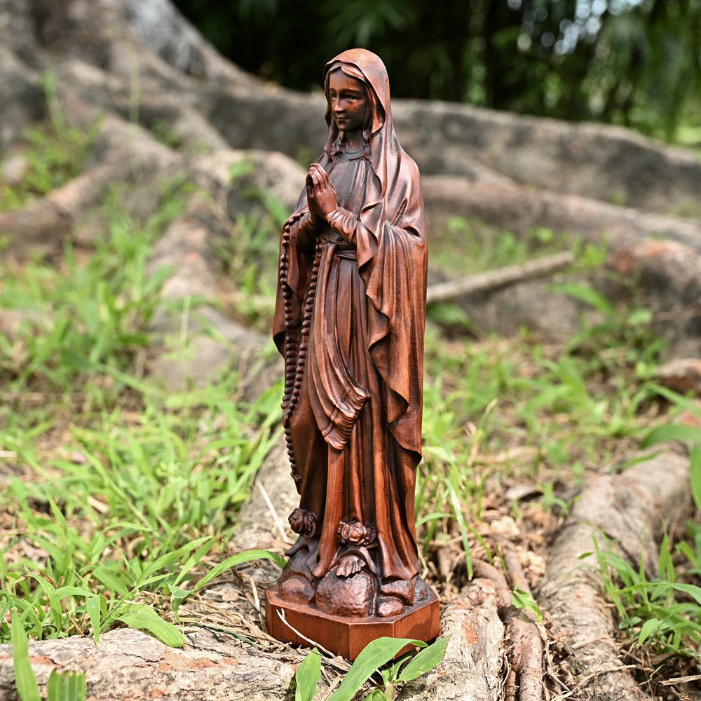 Lourdes Virgin Mary wooden statue displayed outdoors showing detailed religious carving and rosary design