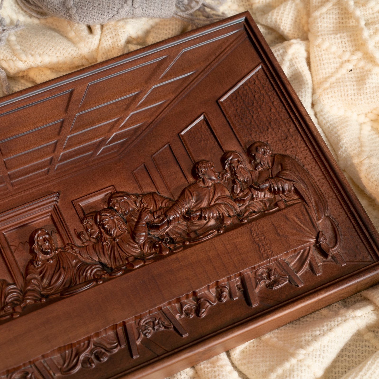 Corner detail of a carved Last Supper wooden plaque showing the framed border and sculpted table scene