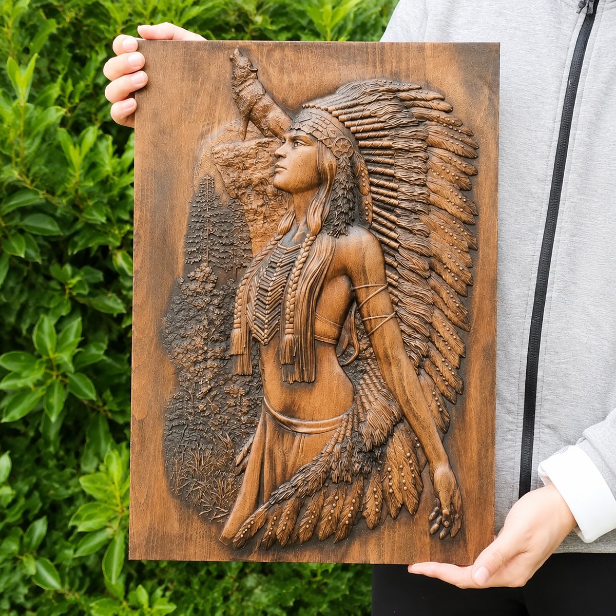 Handmade wooden relief plaque showing a Native American woman with feather headdress and wolf, held by hand outdoors